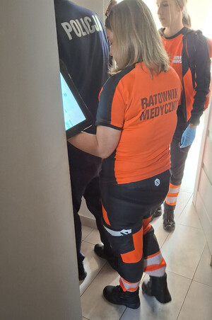 Dwie ratowniczki medyczne i policjant w mieszkaniu kobiety.