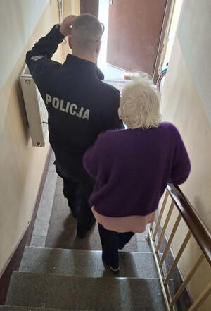 Policjant sprowadza po schodach starszą kobietę.