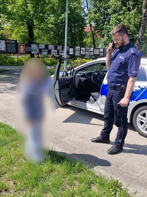 Policjant stoi przy radiowozie obok dziewczynki.