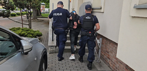 Dwaj policjanci prowadzą zatrzymaną osobę po schodach do budynku.