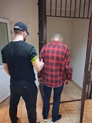 Policjant z zatrzymanym przed okratowanym pomieszczeniem.
