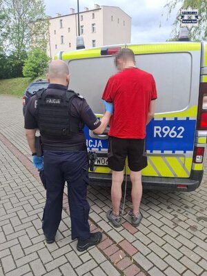Policjant z zatrzymanym przy radiowozie.