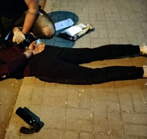 Policjant trzyma zatrzymanego leżącego w kajdankach na ziemi.
