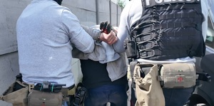 Dwaj policjanci prowadzą skutego kajdankami zatrzymanego.