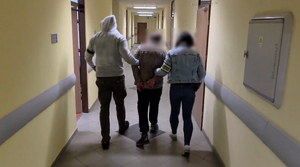 dwóch policjantów prowadzi zatrzymanego przez korytarz.