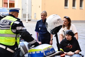 Dziewczynka z mamą i policjantka stoją przed funkcjonariuszem przy motorze.