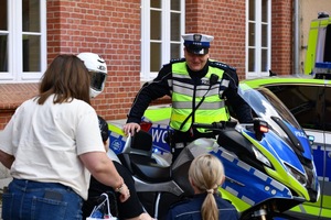 Dziewczynka z mamą i policjantka stoją przed funkcjonariuszem przy motorze.