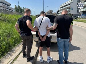 Dwaj policjanci z zatrzymanym mężczyzną przy samochodzie.