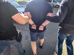 Zatrzymany mężczyzna prowadzony przez policjantów.
