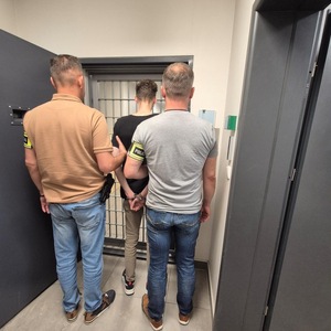 Dwaj policjanci z zatrzymanym w kajdanki.