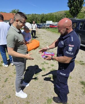 Policjant wręcza mężczyźnie z dzieckiem na ręku czekolady.