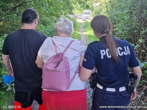 Policjantka i ratownik prowadzą kobietę.