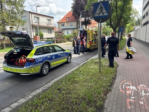 Karetka i radiowóz policyjny stoją na ulicy. Na chodniku obok grupa policjantów.