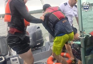Policjant z mężczyzna wciągają człowieka z wody do łódki.