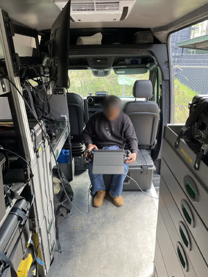 Policjant siedzi  aucie i na kolanach trzyma laptopa.