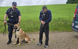 Policjant z psem na smyczy. Obok mężczyzna w kajdankach.