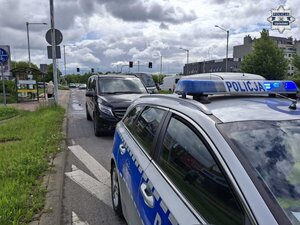 Na pierwszym planie radiowóz policyjny, a za nim stoi karawan zatrzymany przez policjantów.