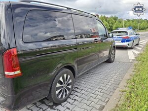 Na pierwszym planie widziany od tyłu bok karawanu, a za nim radiowóz policyjny.