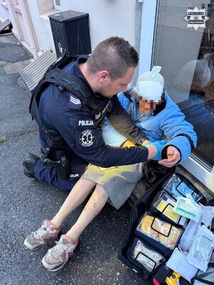 Policjant udziela kobiecie pomocy przedmedycznej.
