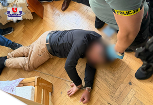 na podłodze leży zatrzymany. nad nim stoi policjant.