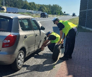 Policjanci wymieniają koło  w samochodzie.