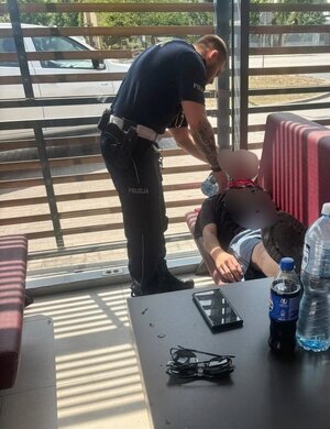 Policjant podaje wodę leżącemu na ławce mężczyźnie.