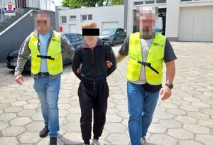 Dwaj policjanci prowadzą przez parking zatrzymanego.
