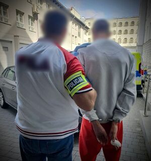 Policjant z zatrzymanym mężczyzną zakutym w kajdanki.