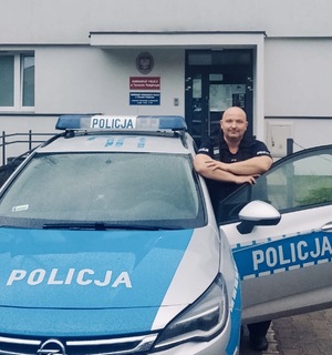 Policjant stoi przy radiowozie z otwartymi drzwiami.
