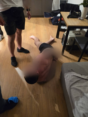 Wnętrze mieszkania. Zatrzymany leży na podłodze skuty w kajdanki. Obok stoi funkcjonariusz.