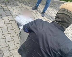 Zatrzymany leży na ziemi, obok stoi funkcjonariusz.