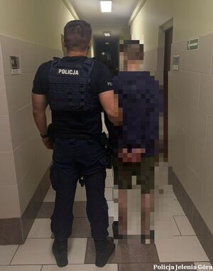 Policjant prowadzi zatrzymanego korytarzem.