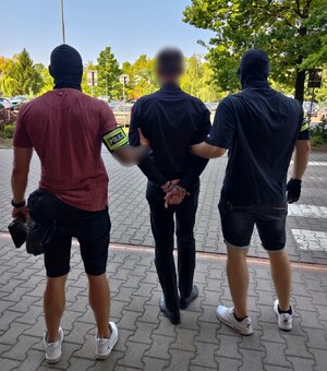 Dwaj ubrani po cywilnemu policjanci prowadzą zatrzymanego - widok z tyłu.