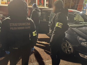 Policjant i funkcjonariusz Straży Granicznej przy nieoznakowanym  radiowozie.