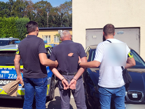 Dwaj funkcjonariusze trzymają zatrzymanego mężczyznę.