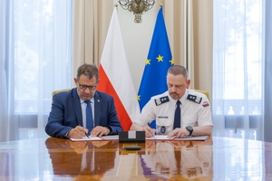 Szef Krajowej Administracji Skarbowej  Marcin Łoboda oraz Komendant Główny Policji gen. insp. Marek Boroń podpisują porozumienie siedząc przy stole.