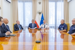 Uczestnicy uroczystości podpisania porozumienia siedzą przy stole.
