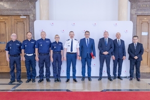 Uczestnicy uroczystości podpisania porozumienia stoją pozując do zdjęcia na tle ścianki z logo KAS.