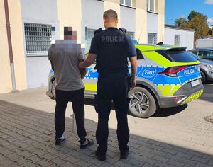 Policjant stoi z zatrzymanym mężczyzną przy radiowozie.