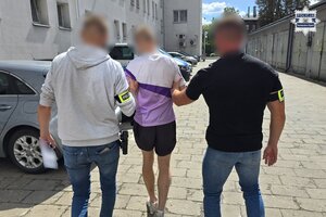 Dwaj policjanci prowadzą zatrzymanego zakutego w kajdanki.