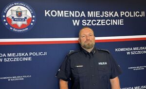 Umundurowany policjant pozuje na tle ścianki z napisem: Komenda Miejska Policji w Szczecinie.