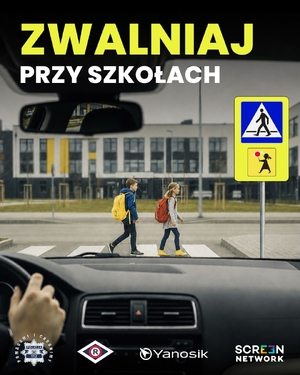 Plakat z napisem zwalniaj przy szkołach. W tle dwoje dzieci na przejściu dla pieszych widziane przez szybę samochodu zbliżającego się do tego przejścia. Dzieci mają na plecach tornistry.