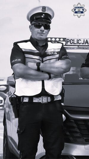 Mł. asp. Robert Foltyniak stoi przy radiowozie.