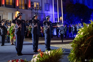 Trzej zastępcy komendanta głównego Policji oddają hołd poległym policjantom przed obeliskiem na terenie Komendy Głównej Policji. W tle uczestnicy uroczystości stojący przed budynkiem KGP.