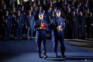 Policjant i policjantka niosą zapalone znicze.