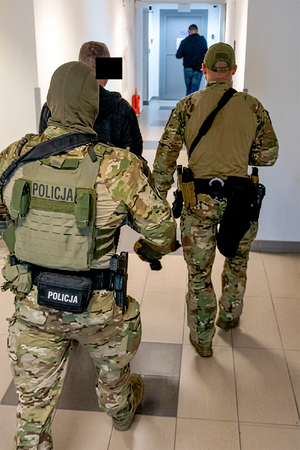 Policjanci prowadzą korytarzem zatrzymanego.