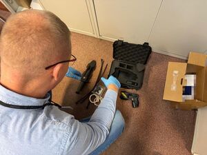 Policjant kuca przy walizce z paralizatorem.