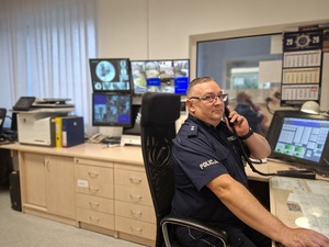 Dyżurny sępoleńskiej jednostki, podkom. Igor Kurczych na stanowisku kierowania, siedzi na krześle, przy uchu trzyma słuchawkę telefonu.