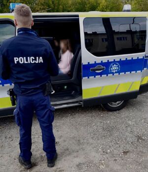 Policjant stoi przy radiowozie, w którym siedzą dwie dziewczynki.