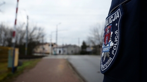 Widoczny rękaw policjanta z naszywką, a w oddali widać przejazd kolejowy.